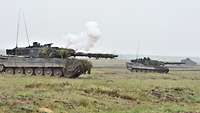 Zwei Kampfpanzer und ein Schützenpanzer überqueren ein grünes Feld.