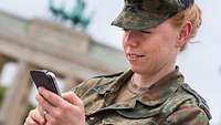 Ein Soldatin in Uniform steht mit einem Mobiltelefon in der Hand vor dem Brandenburger Tor in Berlin.