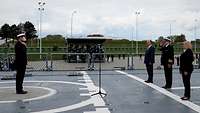Fregatte Sachsen-Anhalt Meldung Indienststellung Auf dem Flugdeck eines Kriegsschiffes salutiert ein Marineoffizier in dunkelblauer Uniform vor drei weiteren Personen.