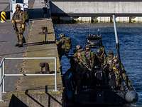Mehrere Soldaten in Flecktarnuniform steigen aus einem Boot auf eine Kaimauer in einem Hafen.