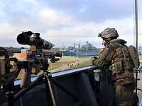 Ein Soldat in Flecktarnuniform steht in der Nock einer Schiffsbrücke; im Hintergrund eine Rasenfläche mit Weg.