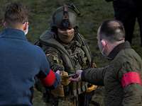 Ein Soldat in Flecktarnuniform reicht zwei postkartengroße Dokument an zwei Männer im Vordergrund.