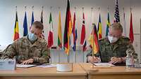 Two soldiers sitting at a table, each signs a copy of the certificate