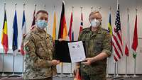 Two soldiers holding a folder with a signed certificate inside