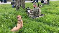 Ein Soldat mit einem Liederbuch und ein Hund sitzen im Gras