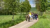 Der Pilgerzug auf dem Weg, angeführt durch einen Fahnenträger