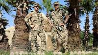 Zwei Soldaten stehen nebeneinander vor mehreren Palmen 