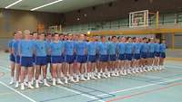 Rekruten in blauer Sportbekleidung sind in der Sporthalle in drei Reihen hintereiander angetreten.