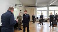 Männliche Person in Arbeitsunifrom der Feuerwehr steht vor weiterer männlicher Person, die aus einer Urkunde vorliest.