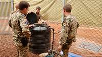 Vier Soldaten stehen um einen runden schwarzen Wasserbehälter, dessen Deckel geöffnet ist