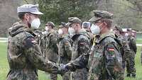 Zwei Soldaten schütteln sich die Hände, inmitten einer Formation. 