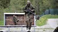 Zwei Soldaten mit Waffen und Marschgepäck überwinden Hindernisse auf der Hindernisbahn.