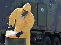 Ein Soldat in Schutzkleidung schüttet Flüssigkeit in einen Behälter