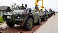 Vier Spähwagen Fennek stehen hintereinander auf Waggons. Auf den Fahrzeugen arbeiten Soldatinnen und Soldaten