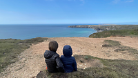 Rückenansicht: Zwei Kinder sitzen auf einem Plateau an der englischen Küste und schauen aufs Meer.