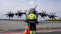 Ein Flughafenmitarbeiter steht mittig vor dem Transportflugzeug A400M und hält Blickkontakt mit den Piloten im Cockpit