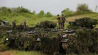 Soldaten stehen auf mit Ästen getarnten Panzern