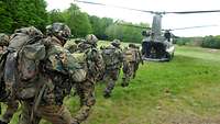 Mehrere Soldaten laufen einen Hubschrauber zu, der am Boden mit geöffneter Heckklappe wartet, um sie aufzunehmen.