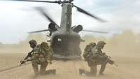 Ein Hubschrauber ist gelandet, die Heckklappe offen. Drei Soldaten sichern hockend mit ihren Waffen im Anschlag.