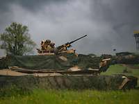 Steadtfast Defender 2021 Kampfpanzer M1A2 Ein Panzer mit Tarnnetzen und mit zwei Soldaten in Tarnfleckuniform im Turm auf einer grünen Wiese.