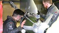 Zwei Soldaten befestigen vorsichtig die Übungsmunition am Eurofighter.