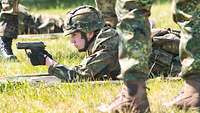 Ein Soldat liegt auf einer Wiese und hält eine Pistole im Anschlag.