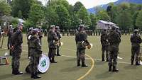 Militärmusiker stehen mit ihren Instrumenten auf einem Appellplatz, auf dem zahlreiche Soldaten angetreten sind.