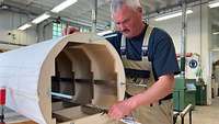 Ein Schreiner arbeitet an einem Flugzeugmodell aus Holz.