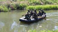 Sieben Soldaten sitzen auf einem Schlauchboot und überqueren ein Gewässer.