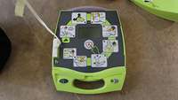 Ein Defibrillator von oben; zu sehen sind die einzelnen Schritte der Maßnahmen in Form von kleinen Bildern