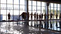 Soldaten in Badebekleidung stehen in einer Schwimmhalle am Beckenrand, einer springt ins Becken.