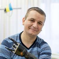 Ein Mann mit einer Armprothese sitzt auf einem Krankenhausbett und lächelt in die Kamera