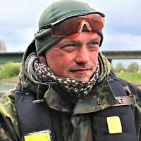 Ein Soldat im Porträt mit Regenjacke und Schwimmweste am Steuer eines Schlauchbootes