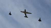 Eine Transall und links und rechts neben ihr jeweils ein Eurofighter fliegen Formation.