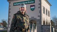 Ein General steht vor einer Kaserneneinfahrt, über seinem Kopf im Hintergrund der Schriftzug Infanterieschule