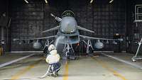 A person kneeling in front of a gray aircraft and spraying water into the engines