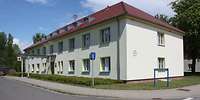 Ein zweistöckiges, helles Gebäude mit eine Walmdach