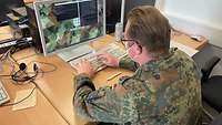 Eon Soldat sitzt an einem Computer und tippt etwas auf der Tastatur.