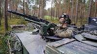 Eine Soldatin an der Waffe in der Panzerluke stehend im Wald