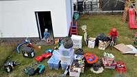 Luftbild: Vor einem Haus stehen Plastikkisten, Pappkartons und Gegenstände, dazwischen zwei Kinder.