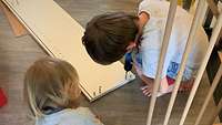 Blick von oben. Zwei Kinder hocken neben einem Brett, der Junge hält einen Schraubendreher.