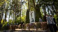Mehrere Soldaten in Dienstanzug und zwei Zivilisten stehen um ein Denkmal im Wald.