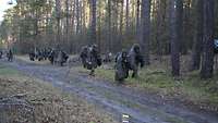 Soldaten laufen am Rande eines Waldweges mit ABC-Schutzmasken und -umhängen und Gefechtshelmen.