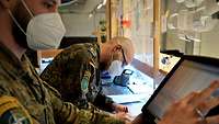 Zwei Soldaten stehen am Empfang der Einsatzkantine. Einer tippt auf eine Kasse, der Soldat im Hintergrund schreibt