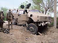 Soldaten stehen vor einem zerstörten Transportfahrzeug Dingo