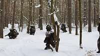 Vier Soldaten hocken in einem verschneiten Wald und richten ihre Waffen in jeweils eine Richtung.