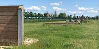 Auf einer Wiese sind mehrere Holz-Metallkonstruktionen mit Abstand hintereinander aufgebaut.