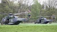 Soldaten besteigen zwei Militärhubschrauber, die auf einer Wiese gelandet sind.