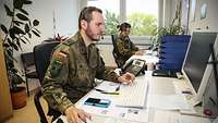 Ein Soldat und eine Soldatin sitzen vor Computern.