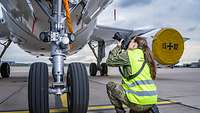Fotosoldatin Miriam Altfelder kniet auf dem Boden und fotografiert von oben nach unten das Fahrwerk eines Flugzeuges.
